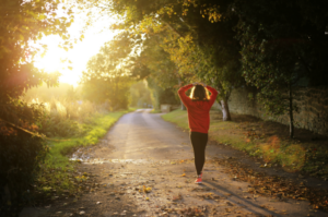 Woman walking down a peaceful tree-lined road during golden hour sunlight.