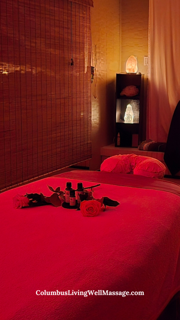 Warmly lit massage therapy room with massage table, aromatherapy oils, rose accents, and Himalayan salt lamps creating a calming wellness atmosphere