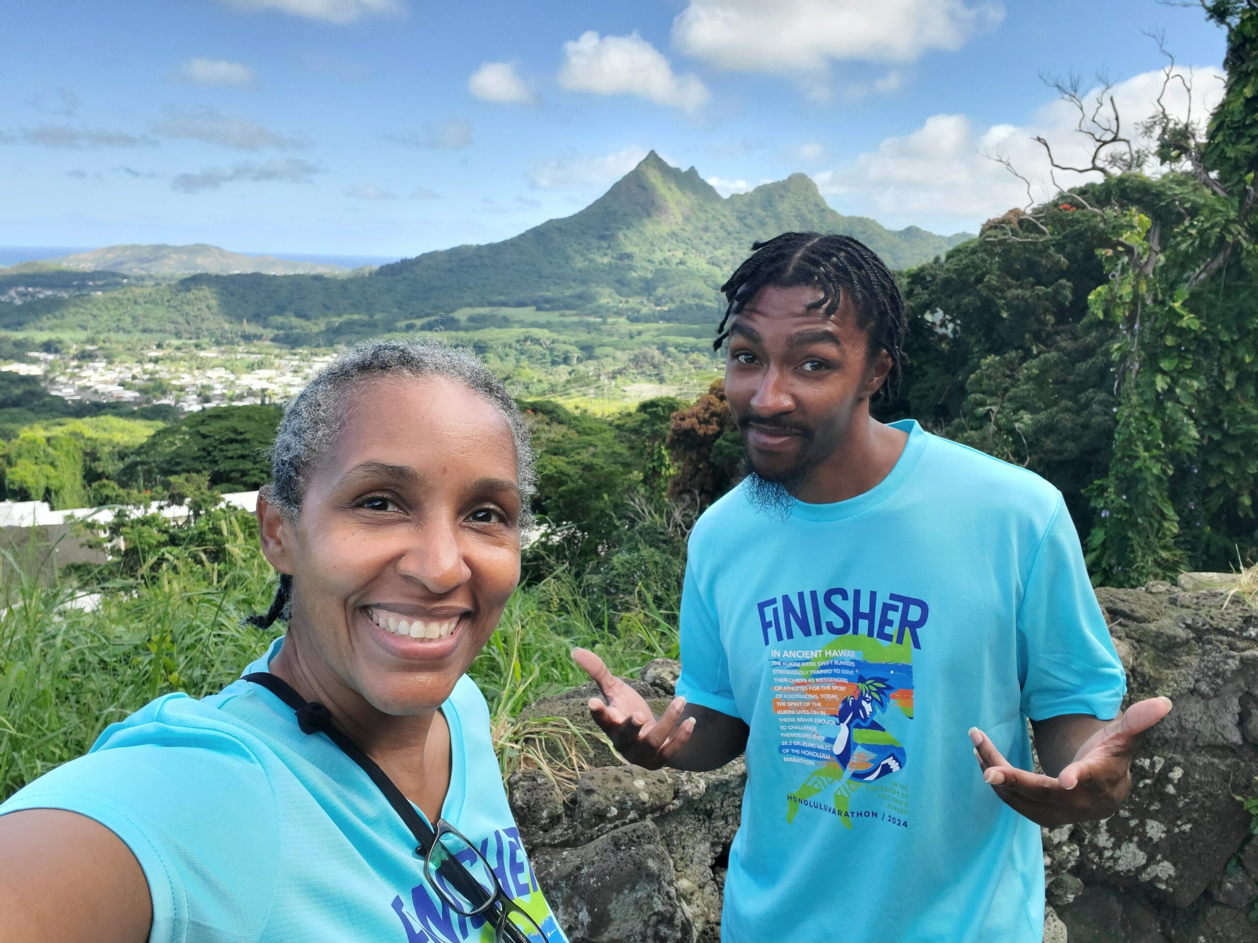 Kimberlee and her son smiling together outdoors after completing the Honolulu Marathon, with mountain scenery in the background.