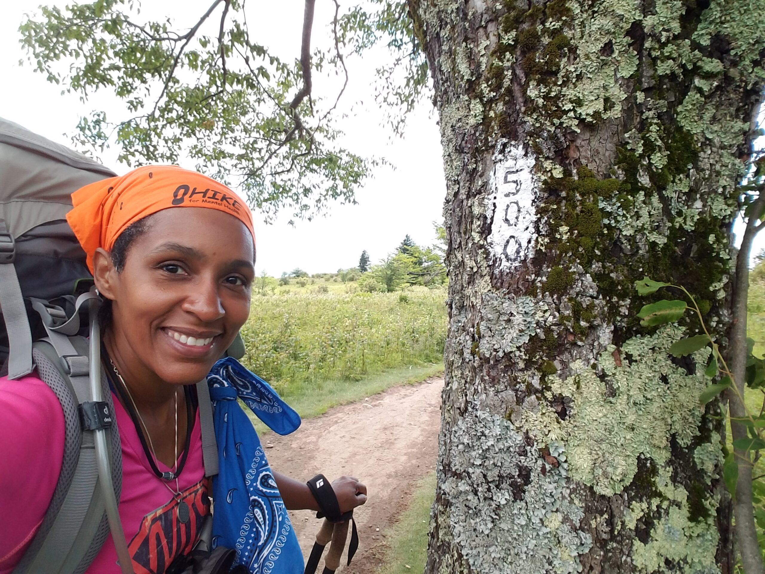 Smiling woman standing beside a 500-mile Appalachian Trail marker during a backpacking journey, symbolizing the progress, confidence, and commitment that grow through consistent effort over time.