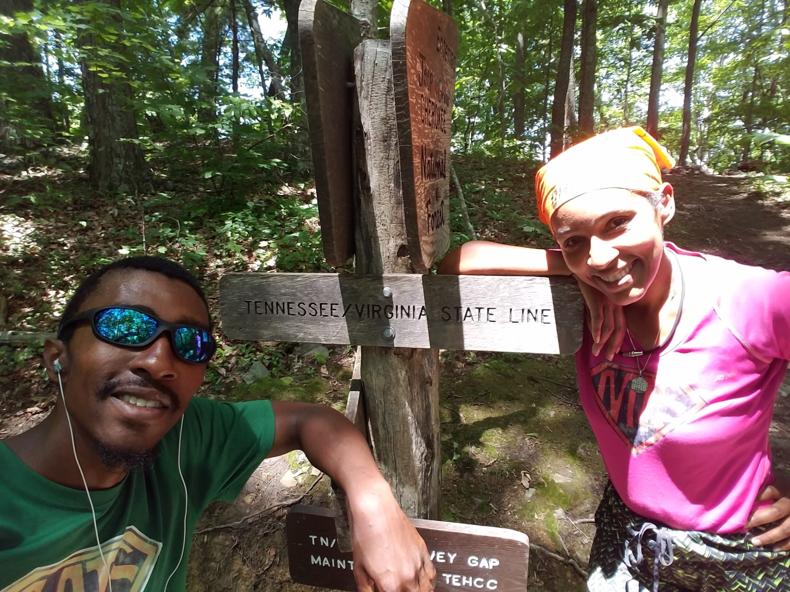Kimberlee and her son smiling beside the Tennessee and Virginia state line sign on the Appalachian Trail during a backpacking trip.
